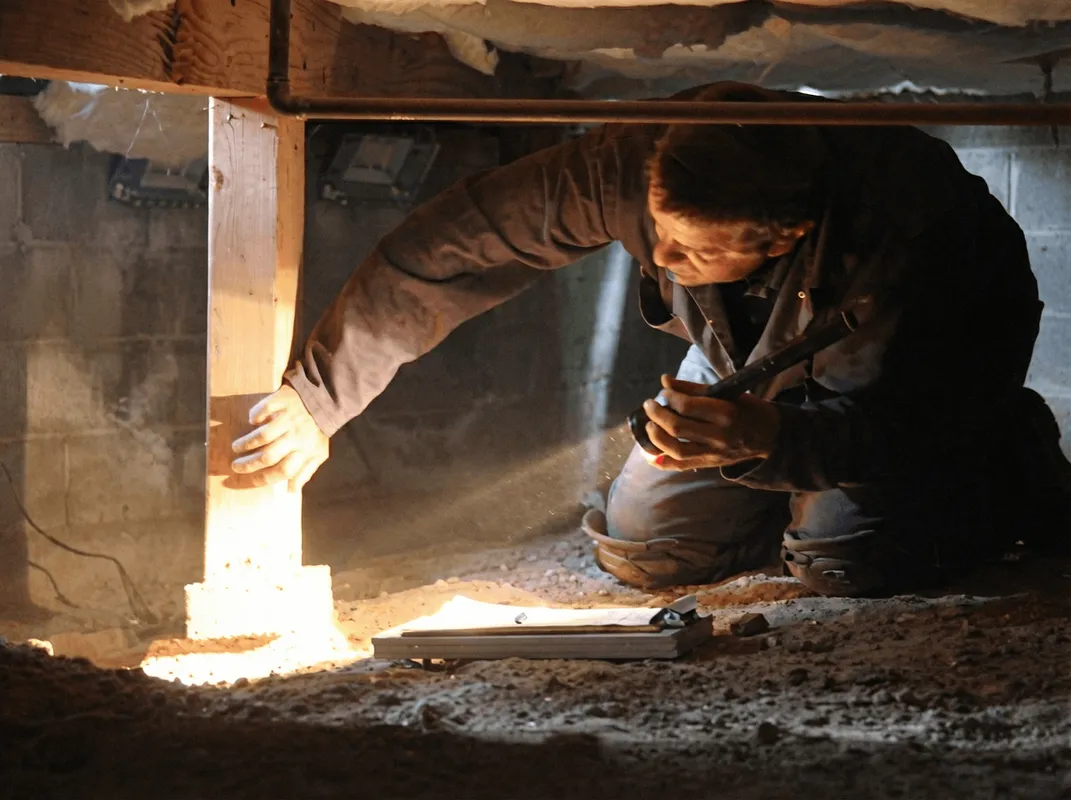 A professional inspecting wooden beams under the floor of a structure in Oklahoma City, OK