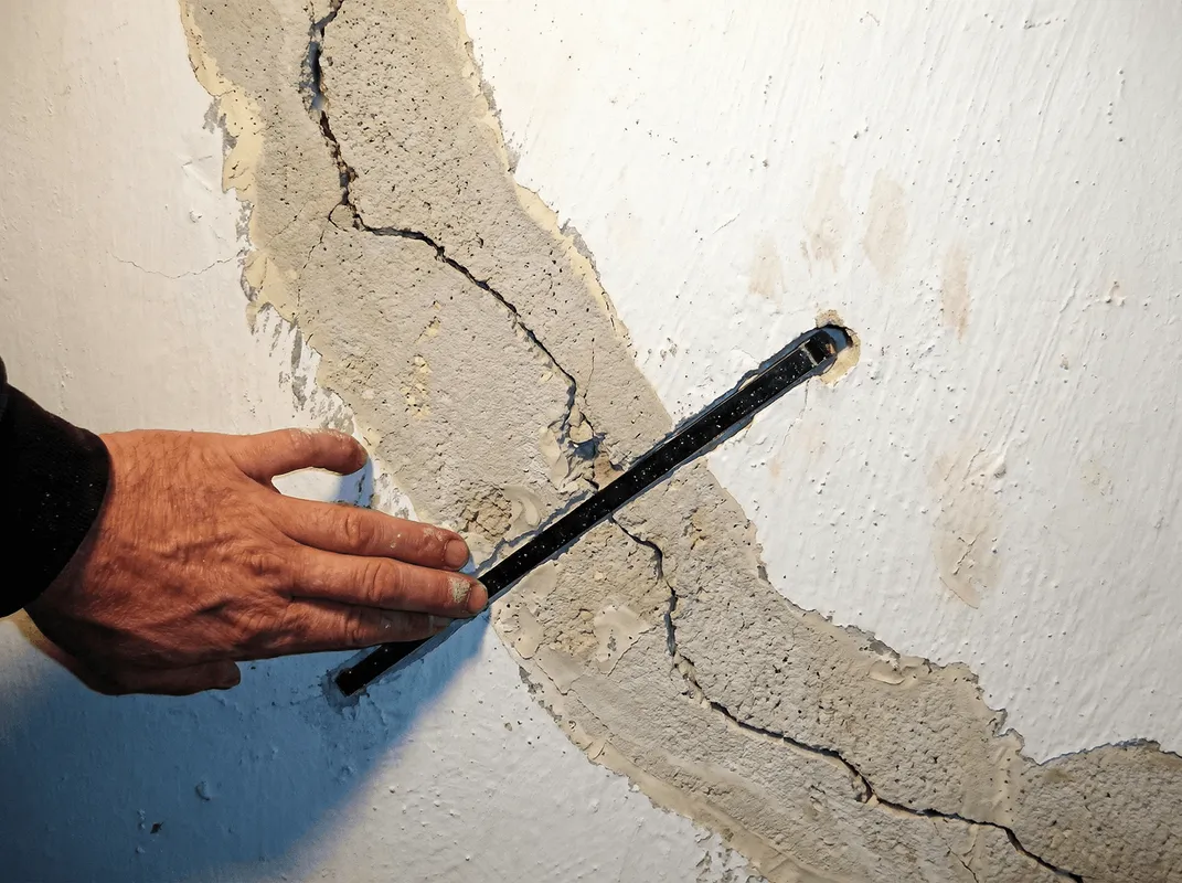 A wall with a large crack is being inspected by a professional in Oklahoma City, OK